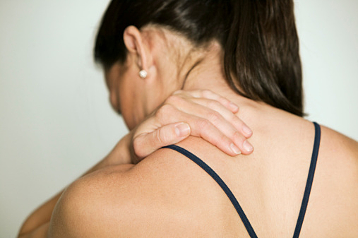 Woman massaging shoulder, in studio, rear view
